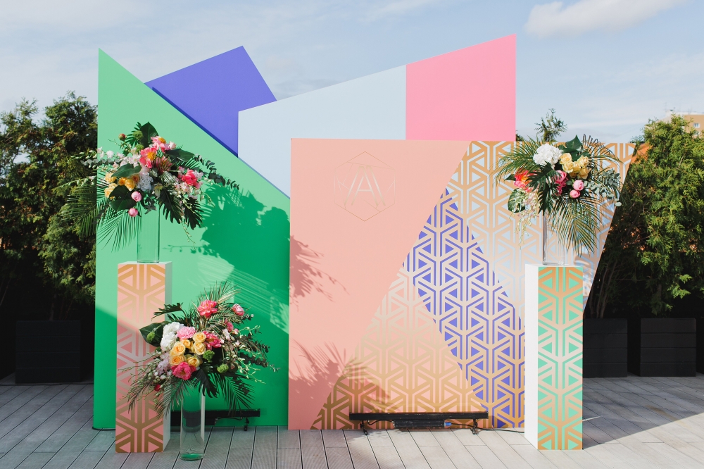 Наши декораторы выстроили целую инсталляцию из разноцветных многоугольников и связали её с оформлением зала с помощью ярких композиций из тропических листьев и цветов.