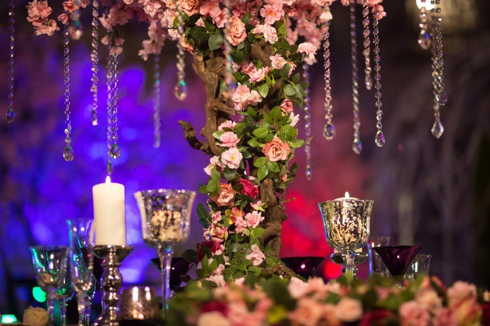 Оформление гостевого стола на ночной свадьбе. Стол украшен цветущим деревом с повесами из кристаллов. Множество свече создают блики и отражения граней кристаллов.