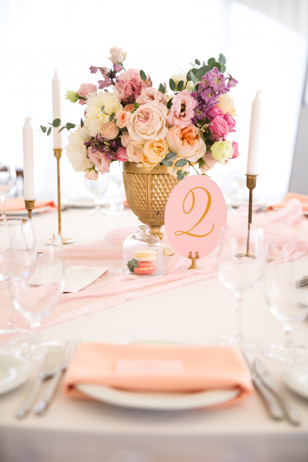Пастельные оттенки во флористике дополняются ноткой золота в декоре. Оформление стола также включало шелковую дорожкой пудрово-розового оттенка, персиковыми салфетками и пирожными макаронс в небольших стеклянных колпаках.
