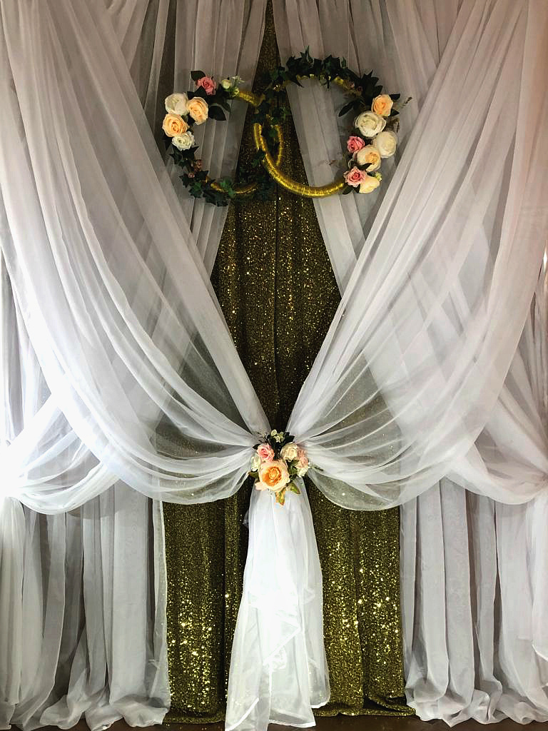 Фотозона, оформлена воздушной вуалью и золотистой драпировкой в центре, используется дополнительный декор в виде цветочных колец.