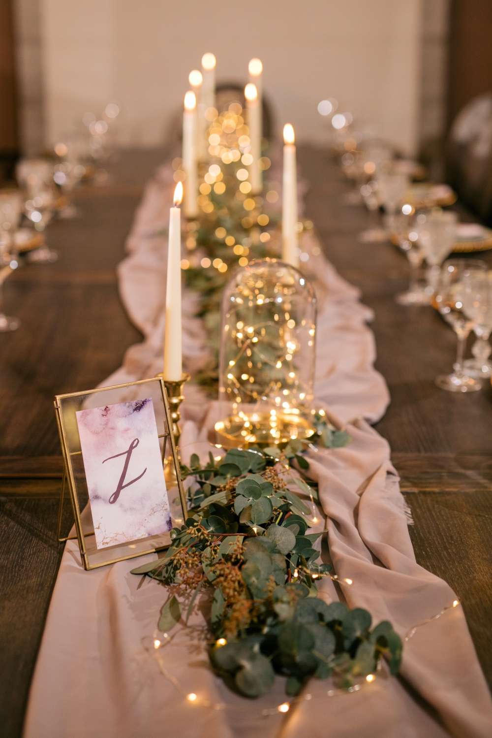Оформление длинного деревянного стола гостей зеленью, свечами и лампочками.